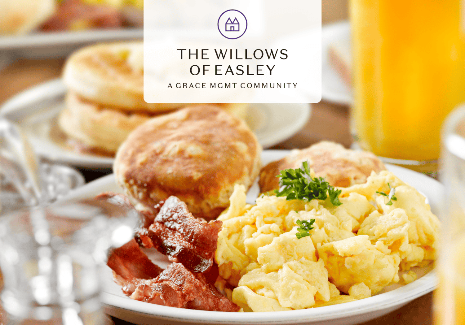 Breakfast plate with scrambled eggs, bacon, biscuits, and parsley on a table; orange juice in the background with a logo overlay.